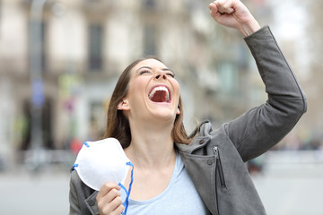 Excited woman celebrating holding mask on city street