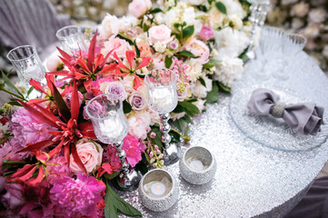 flower arrangement stands on the table in wedding banquet area on a balcony, the table is decorated with candles, there are plates, glasses, cutlery