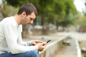 Side view of serious adult man using phone in a park