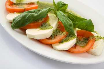 Caprese Salad with Tomatoes, Mozzarella Cheese, Rocket Salad, basil leaves, dressed with Pesto Sauce on rustic wooden background.  Traditional Italian cuisine. Flatlay healthy vegetarian dish.