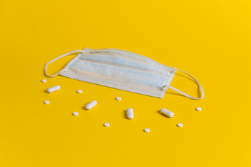 Protective medical mask on yellow background surrounded with white pills. Creative concept of healthcare, hygiene, virus protection and medical treatment on coronavirus quarantine