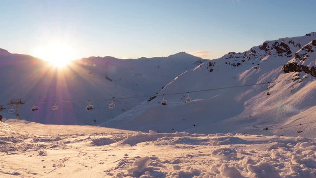 Timelapse of the sun setting behind a mountain landscape with a ski lift in front 