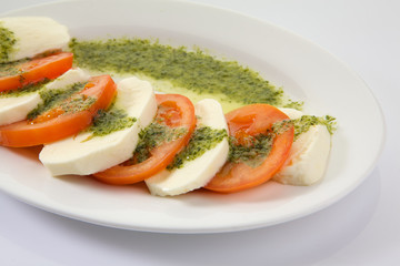 Caprese Salad with Tomatoes, Mozzarella Cheese, Rocket Salad, basil leaves, dressed with Pesto Sauce on rustic wooden background.  Traditional Italian cuisine. Flatlay healthy vegetarian dish.