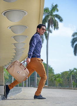 Modelo ingeniero saliendo corriendo de la empresa con maletín en el portal del teatro Nacional de Cuba con pantalón amarillo mostaza y gafas de Sol camisa de mangas largar con pose