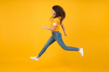 Fototapeta na wymiar Feel inner energy. Pretty girl with long hair. Fashion style. Beauty and make up. Energetic woman running or jumping. Skinny jeans suits her. Sexy girl yellow background. Sensual girl in casual style