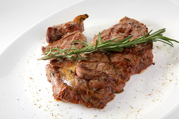 Grilled beef steak with rosemary. Grilled striploin sliced steak. Juicy thick grilled T-bone beef steak seasoned with rosemary fresh of the summer BBQ. Vegetables on a black plate with salt and pepper