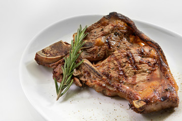 Grilled beef steak with rosemary. Grilled striploin sliced steak. Juicy thick grilled T-bone beef steak seasoned with rosemary fresh of the summer BBQ. Vegetables on a black plate with salt and pepper