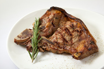 Grilled beef steak with rosemary. Grilled striploin sliced steak. Juicy thick grilled T-bone beef steak seasoned with rosemary fresh of the summer BBQ. Vegetables on a black plate with salt and pepper