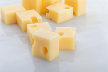 Portions (cubes, dice) of Emmental Swiss cheese with scratcher. Texture of holes and alveoli. On white marble background.