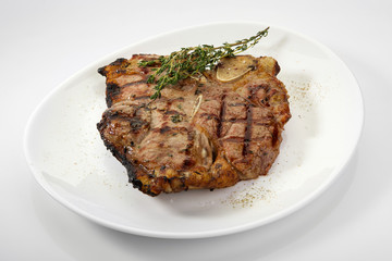 Grilled beef steak with rosemary. Grilled striploin sliced steak. Juicy thick grilled T-bone beef steak seasoned with rosemary fresh of the summer BBQ. Vegetables on a black plate with salt and pepper