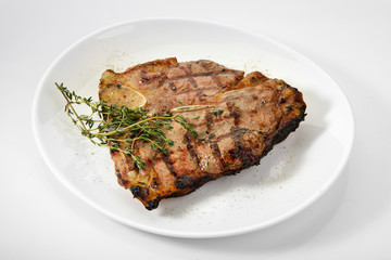 Grilled beef steak with rosemary. Grilled striploin sliced steak. Juicy thick grilled T-bone beef steak seasoned with rosemary fresh of the summer BBQ. Vegetables on a black plate with salt and pepper