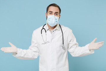 Perplexed confused male doctor man in white medical gown sterile face mask gloves isolated on blue background. Epidemic pandemic coronavirus 2019-ncov sars covid-19 flu virus concept. Spreading hands.