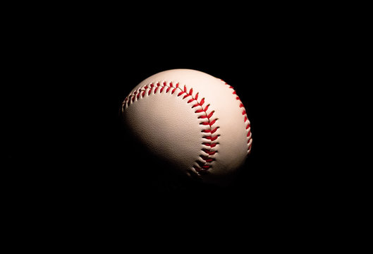 A close up of a white and red base ball in the dark with black background