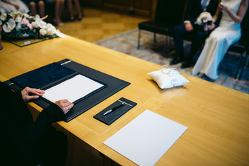 bride and groom sit in the municipality at the state registrar. the registrar keeps his hand on the...