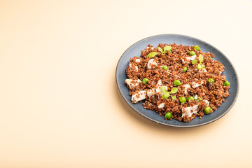 Quinoa porridge with green pea and chicken on ceramic plate on a pastel orange background. Side view, copy space.