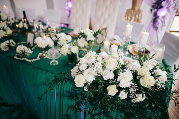 decoration of white flowers, greenery, candles are on a festive table with a green cloth