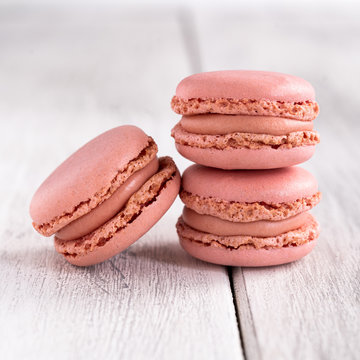 Pink tasty macaroons stacked in pile against wooden white surface