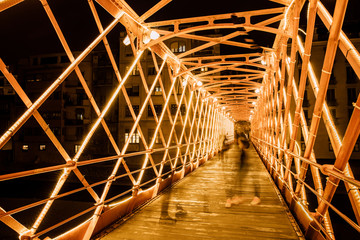 Metal illuminated bridge construction and people walking on bridge in Girona, Catalonia, Spain