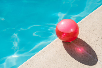 Red ball on the edge of swimming pool on summertime