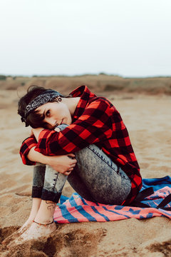 Thoughtful hipster woman sitting on sandy beach