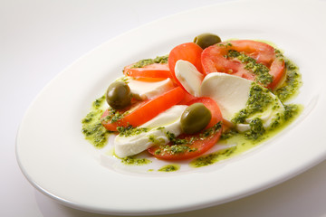 Caprese Salad with Tomatoes, Mozzarella Cheese, Rocket Salad, basil leaves, dressed with Pesto Sauce on rustic wooden background.  Traditional Italian cuisine. Flatlay healthy vegetarian dish.