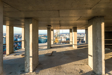 Interior of a concrete residential apartment building room with unfinished bare walls and support pillars for future walls under construction.