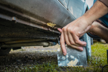 Detail of an amateur mechanic applying polyester putty to repair the sill of his beat up rusty car. Fixing underside of a car with putty.