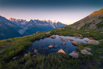 From above small clear lake with stone on bottom reflecting sky high in mountains in Chamonix, Mont-Blanc