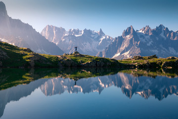 Lonely tourist on hilly shore reflecting in crystal lake in snowy mountains in sunlight