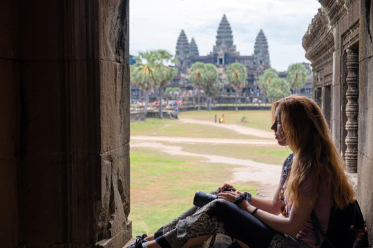Side view of concentrated young woman with camera contemplating ancient religious temple while resting in Angkor Wat in Cambodia 