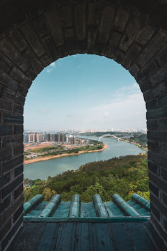 Fototapeta Shot through brick old window with view of cityscape of Nanning on river shore, China