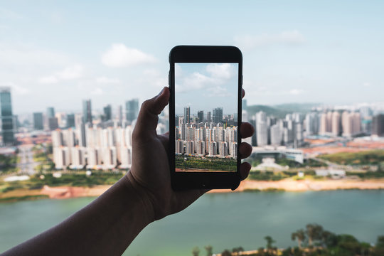 Crop hand holding smartphone and taking picture of contemporary city of Nanning from height, China
