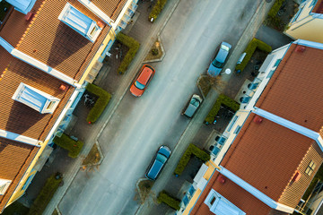 Obraz premium Aerial view of residential houses with red roofs and streets with parked cars in rural town area. Quiet suburbs of a modern european city.
