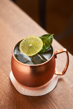 From above classic alcohol cocktail Moscow Mule based on vodka with ginger beer and lime juice served in copper mug decorated with lemon slice on wooden table