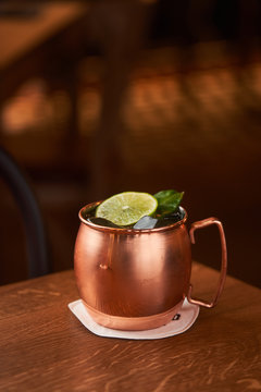 Classic alcohol cocktail Moscow Mule based on vodka with ginger beer and lime juice served in copper mug decorated with lemon slice on wooden table