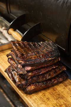Composed stack of grilled juicy ribs on cutting board near barbecue