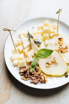 From above of square pieces of cheese with skewers decorated with fresh mint and slices of pear with walnut in restaurant