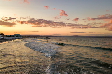 Sea surface with blue water waves under yellow and purple sunset sky.