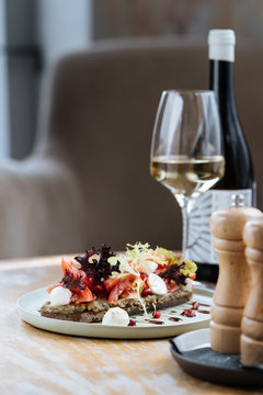 Delicious rye bread smeared with sauce and served with slices of tomatoes colorful lettuce and cheese on table with glass of wine in restaurant