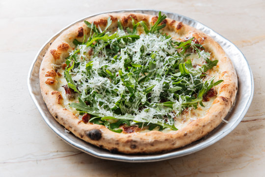 Closeup From Above Of Tasty Baked Pizza Decorated With Green Arugula And Grated Cheese In Restaurant