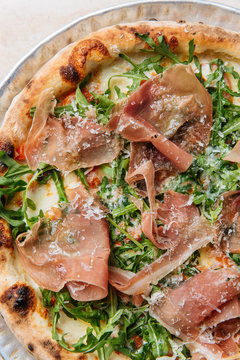 Top view of tasty pizza with thin slices of bacon and fresh greenery on plate in restaurant