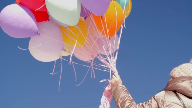 Low angle view of woman holding bunch of balloons. Colorful air balloons against blue sky. Celebration concept