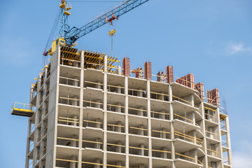 Fototapeta premium Concrete frame of tall apartment building under construction and tower crane in a city.