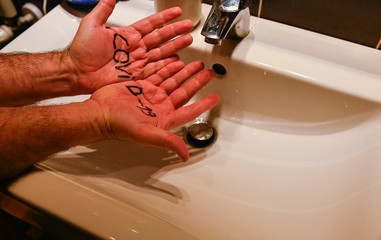 Coronavirus. Conceptual image of the danger of the virus: an inscription on the palms of the hands of a Caucasian man highlights how it attacks man. In the background, a sink for washing and cleaning.