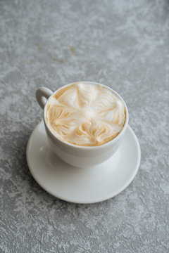 Top view of cup of hot cappuccino with latte art served on white saucer on light grey textured background