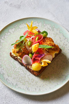 From above tasty sandwich decorated with sliced vegetables and flowers and placed on plate on white table in cafe