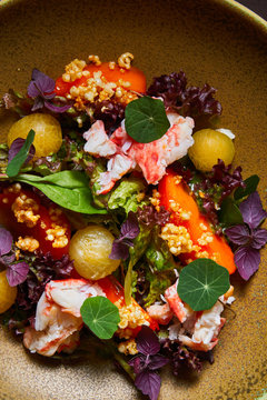 Top view of bowl with delicious crab salad with fresh vegetables and herbs placed on brown table