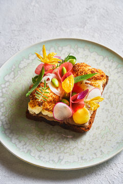 From above tasty sandwich decorated with sliced vegetables and flowers and placed on plate on white table in cafe