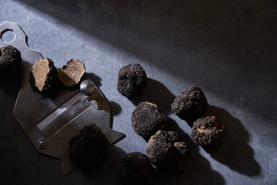 From above bunch of expensive black truffles placed near metal shaver on gray plaster surface