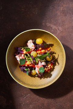 Top view of bowl with delicious crab salad with fresh vegetables and herbs placed on brown table